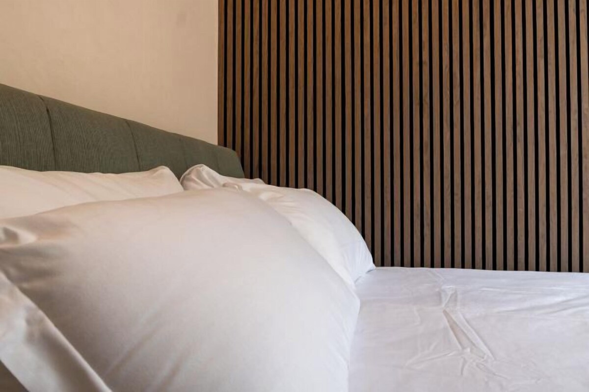A bed with white bedding and a green headboard in a room with vertical wooden paneling.