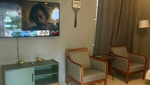 A living room with a television mounted on the wall, two striped armchairs, a green cabinet, and a tennis racket hanging on the wall. - The Polo Club at Racquet Club (Montego Bay)