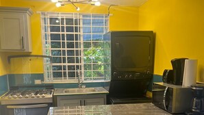 A kitchen with a gas stove, a coffee maker, and a microwave. There are two stools and a window with a view of greenery. - The Polo Club at Racquet Club (Montego Bay)