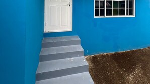A blue building with a white door and window, a set of stairs leading to the entrance, and a small porch area. - The Polo Club at Racquet Club (Montego Bay)