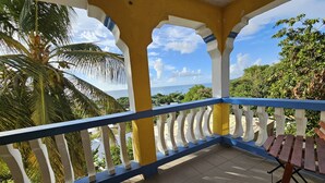 Un balcón con vista al mar, palmeras y un banco de madera.