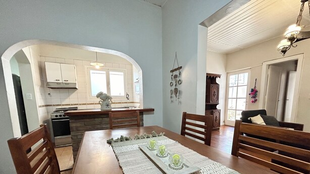 A dining area with a wooden table, chairs, a woven placemat, and a kitchen in the background.