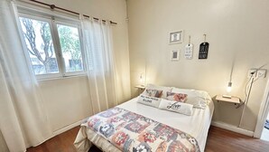 A bedroom with a floral bedspread, a bedside table with a lamp, and a window with curtains.