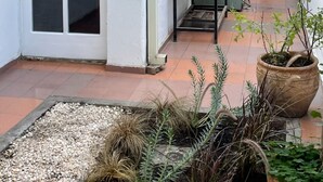 A narrow corridor with a tiled floor, a door with frosted glass panels, a metal rack, and potted plants.