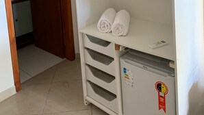 A white storage unit with shelves, a small refrigerator, and a door leading to another room. - Pousada Perola da Praia (Penha)