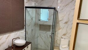 A bathroom with a glass-enclosed shower, a white sink with a marble countertop, and a toilet. - Pousada Perola da Praia (Penha)