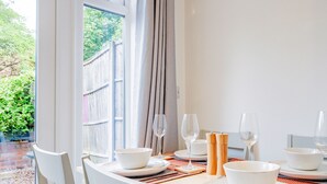 A dining table set with white plates, bowls, and wine glasses, with a view of greenery outside.