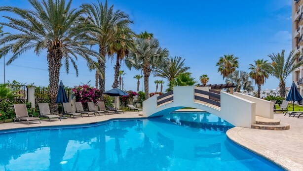 A swimming pool with lounge chairs and umbrellas, surrounded by palm trees.