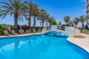 A swimming pool with lounge chairs and umbrellas, surrounded by palm trees.