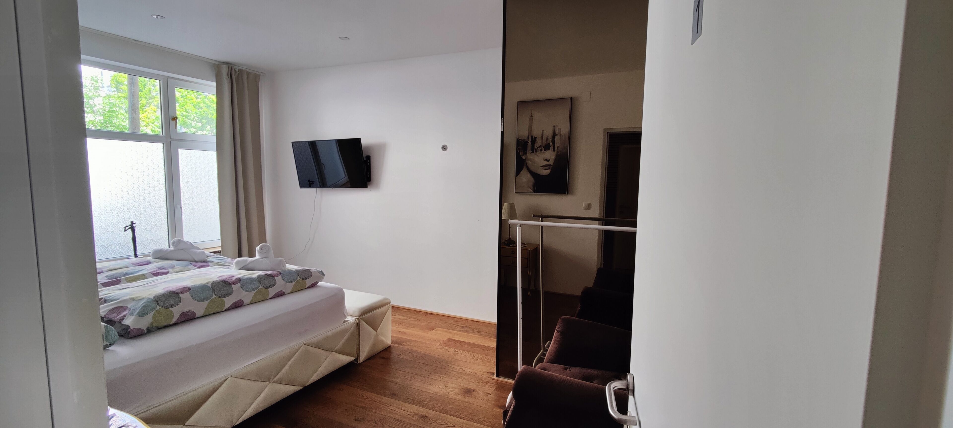 Une chambre à coucher avec un lit, un téléviseur fixé au mur, une fenêtre et un tableau.