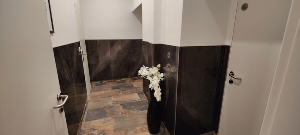 A bathroom with dark marble walls, a tiled floor, and a white vase with flowers.
