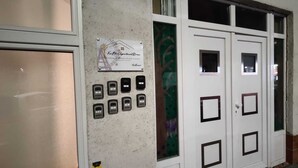 L’entrée d’un hôtel, avec un comptoir de réception, une enseigne indiquant le nom et l’adresse de l’établissement, et une série de sonnettes numérotées.
