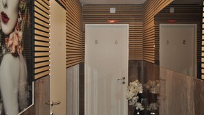Un couloir d’hôtel aux murs recouverts de miroirs, une porte portant les numéros 5 et 6, et un arrangement floral.