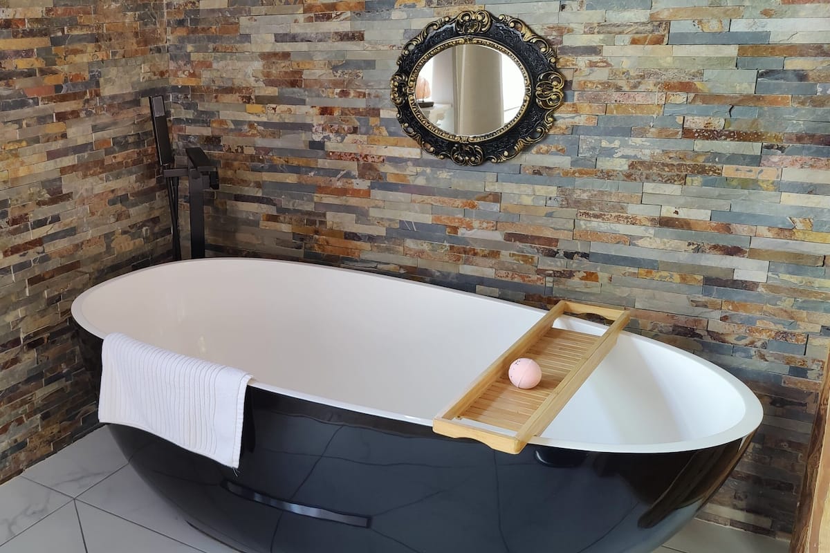 A modern bathroom with a black bathtub, a wooden tray, and a mirror.