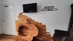 Une pièce avec un escalier en bois, un téléviseur fixé au mur et un porte-manteau.