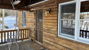 Una cabaña de madera con un porche, una silla de metal y un cartel de ciervo en la puerta.