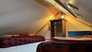 Un dormitorio acogedor en el ático con dos camas, un estante de madera y techo inclinado.