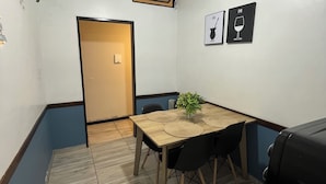 Ett litet mötesrum med ett träbord, svarta stolar, en krukväxt, två väggmonterade fläktar och en svart grill på ett stativ.