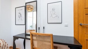 A dining area with a black table, a wicker chair, and two framed artworks on the wall.