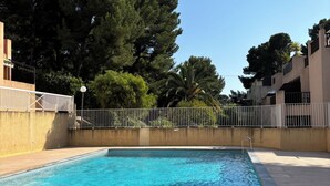 A rectangular swimming pool with clear blue water, surrounded by a concrete deck and a white metal fence. - Appartement à Bandol Avec Piscine et Accès mer (Bandol)