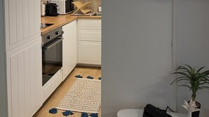 A modern kitchen with white cabinets, a wooden countertop, and a built-in oven. A flat-screen TV is mounted on the wall, and a small table with a potted plant is visible. - Appartement à Bandol Avec Piscine et Accès mer (Bandol)