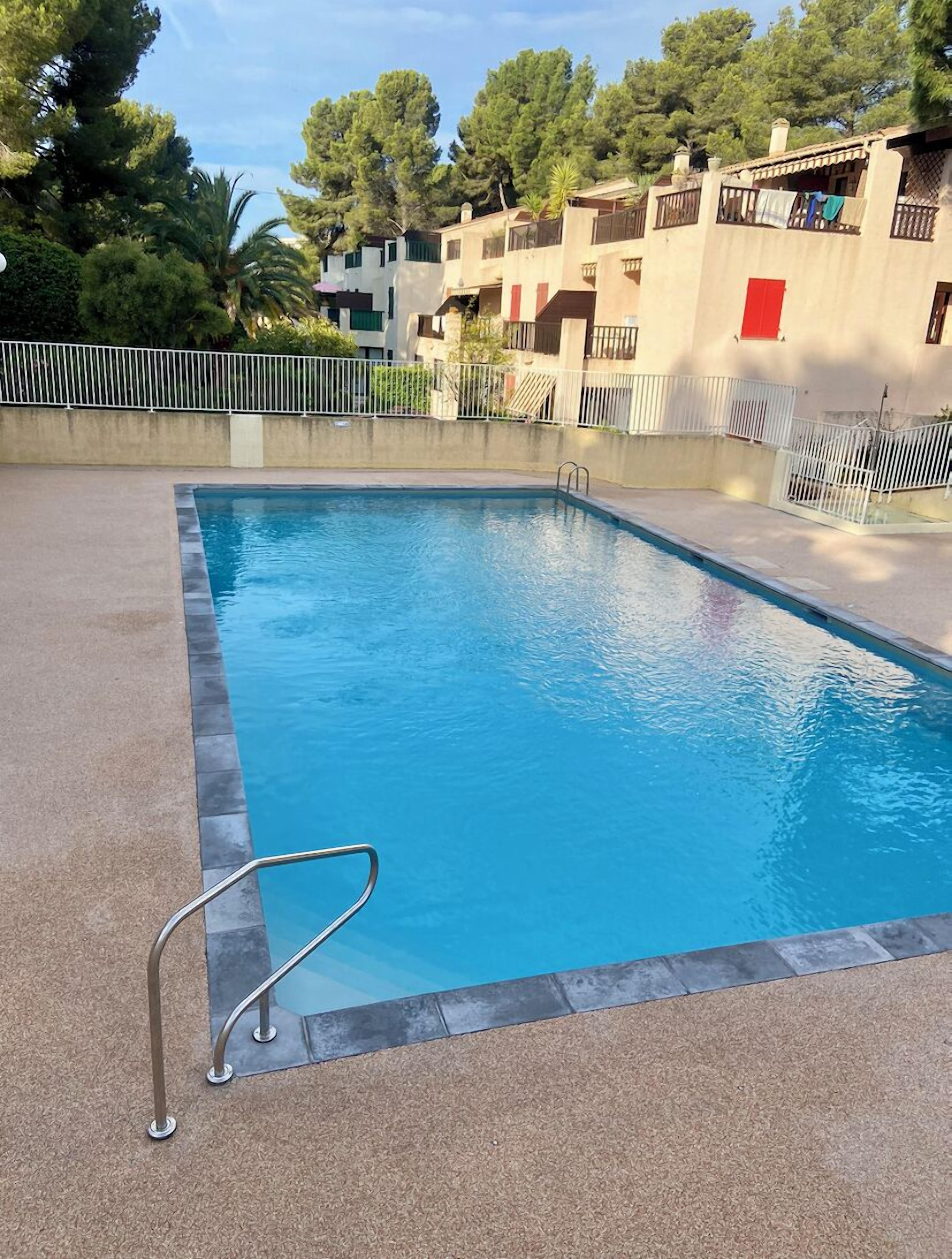 A swimming pool with a metal ladder, surrounded by a concrete deck and a white fence.