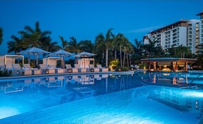 Relax by the tranquil pool, surrounded by palm trees and shaded lounge areas.