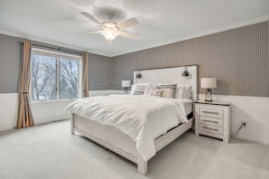 Um quarto com uma cama grande, uma mesa de cabeceira, um ventilador de teto e uma janela com cortinas.