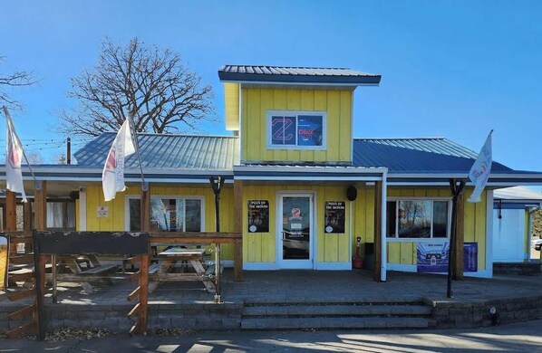 Un bâtiment jaune avec un petit porche et une enseigne sur laquelle on peut lire : « Pizza du mois ».