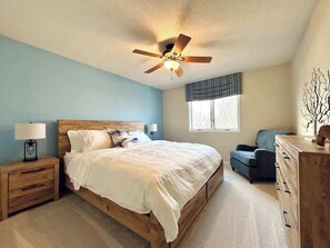 Une chambre à coucher avec un lit en bois, une table de chevet, une commode, une chaise et un ventilateur de plafond.