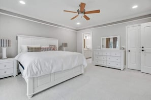 Ein Schlafzimmer mit einem Bett, Nachttischen, einer Kommode, einem Spiegel und einem Deckenventilator.
