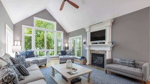 Un salon spacieux avec un haut plafond, de grandes fenêtres, une cheminée et un téléviseur.