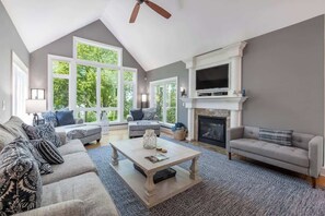 Un salon spacieux avec un haut plafond, de grandes fenêtres, une cheminée et un téléviseur.