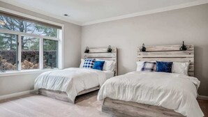 Une chambre avec deux lits, une grande fenêtre et une vue sur les arbres.