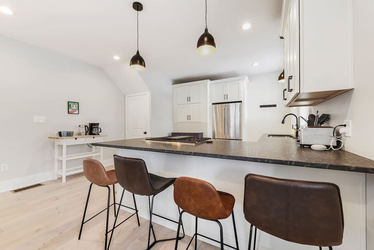 A modern kitchen with white cabinets, a stainless steel refrigerator, and a bar area with stools.