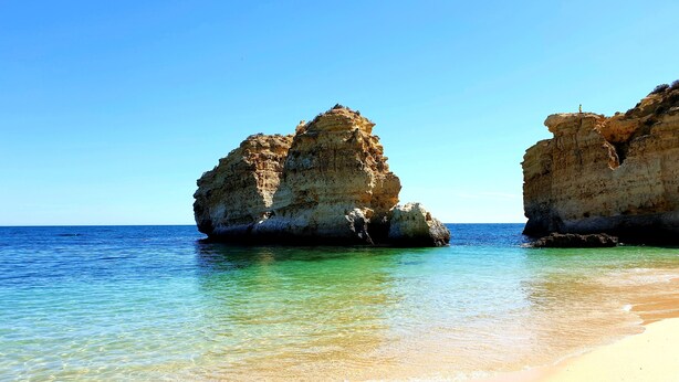 Une plage bordée d’une eau turquoise et limpide et de formations rocheuses.