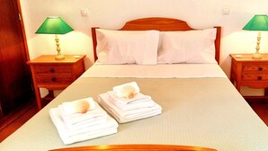 Un lit bien fait, avec du linge de lit blanc, deux tables de chevet avec des lampes et des serviettes pliées posées sur le lit.