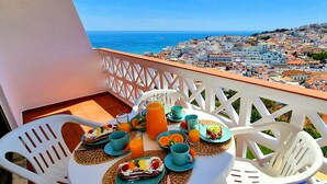 Un balcon avec une table préparée pour le petit-déjeuner, donnant sur une ville côtière.