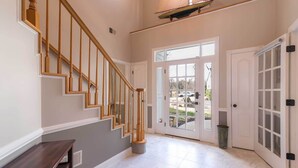 A spacious hallway with a wooden staircase, a large glass door leading outside, and a trash can near the door. - Creek-Side Bliss: Unwind and Create Lasting Memories at Our Beautiful Retreat (Pasadena)
