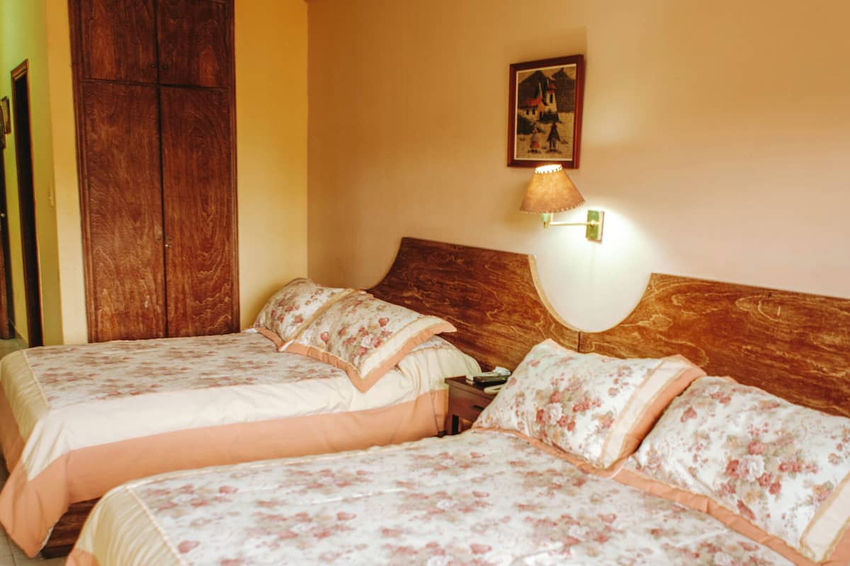 Hotellihuone, jossa on kaksi sänkyä, puiset päätylevyt, yöpöytä ja seinään kiinnitetty valaisin.