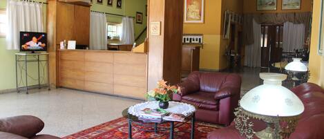Un salón con un mostrador de recepción de madera, sofás de cuero, una mesita con un florero y un televisor sobre un mueble.