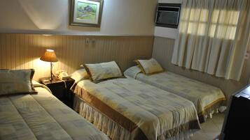 Habitación de hotel con dos camas, una mesita de noche con lámpara, teléfono, un cuadro en la pared y una ventana con cortinas.