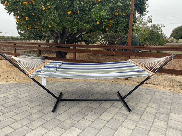 Una hamaca con un cojín a rayas sobre un patio empedrado, bajo un árbol de naranjos.