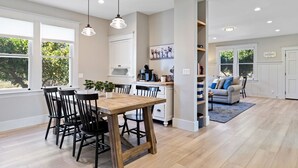 Eine moderne Küche mit einem Holztisch, Stühlen, einer Kücheninsel und Pendelleuchten.