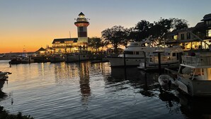 Una marina con barche ormeggiate, un faro e edifici illuminati al tramonto.