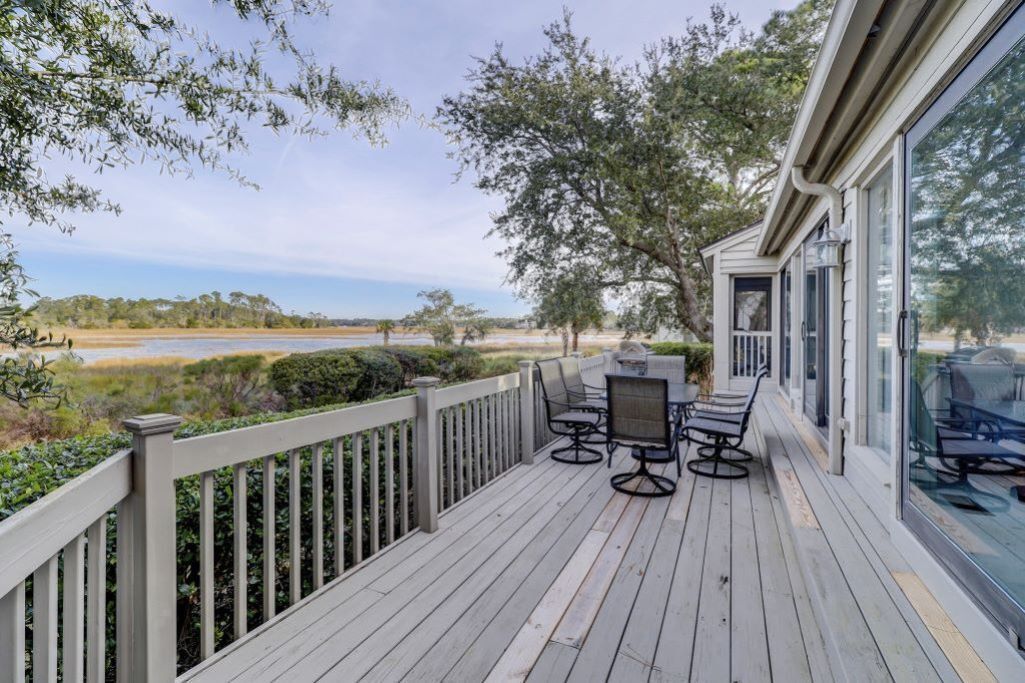 A wooden deck with outdoor furniture, overlooking a natural landscape with trees and a body of water.