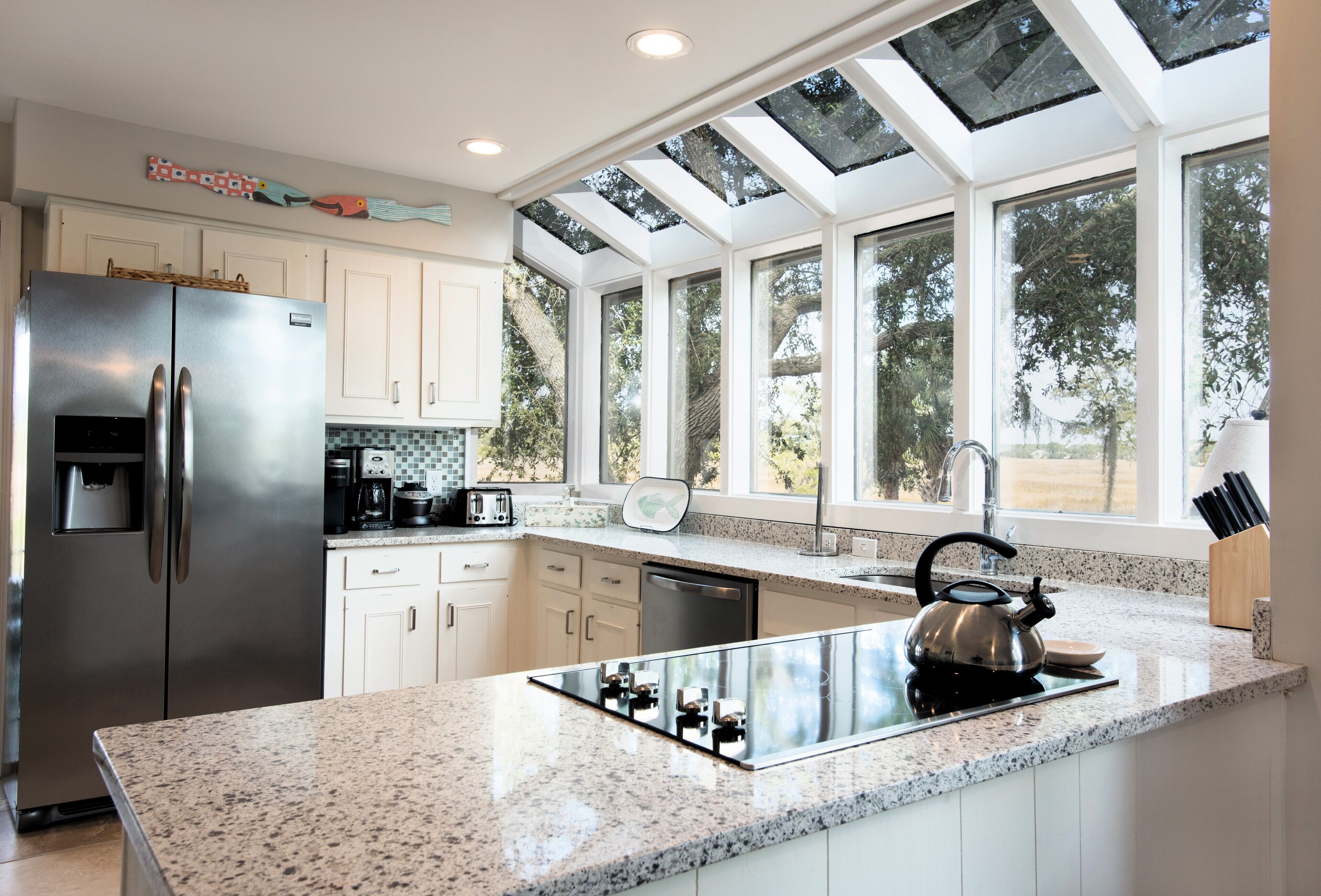 A modern kitchen with a stainless steel refrigerator, a built-in stove, and a large window overlooking a garden.