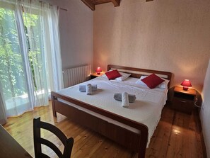 A neatly made bed with white linens and red pillows, a wooden floor, and a window with sheer curtains. - Apartment Suite Agroturist (Rovinj)