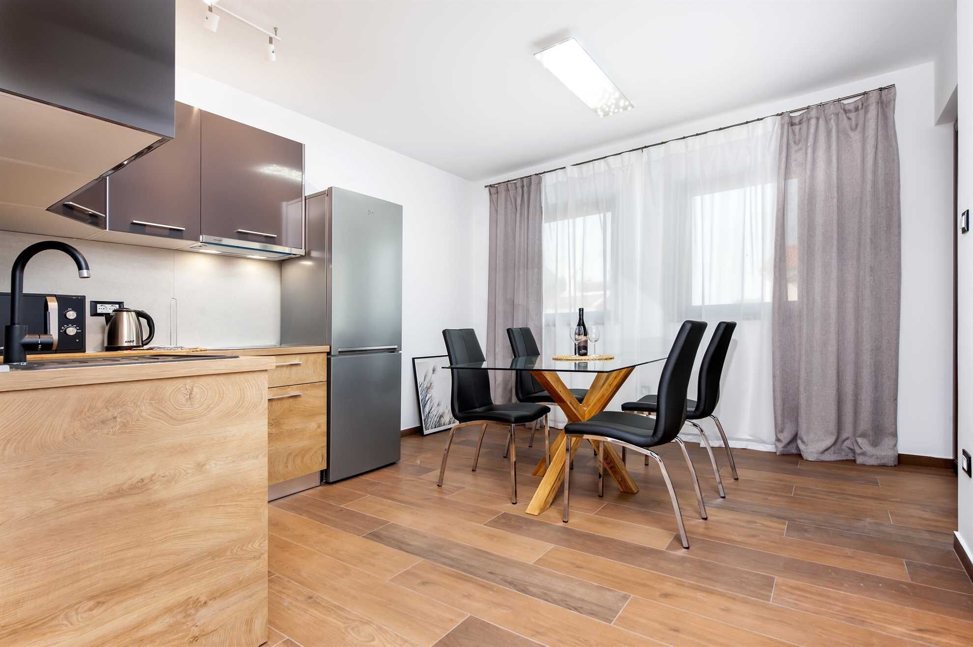 A modern kitchen with a built-in oven, a coffee maker, and a dining area with a glass table and black chairs.