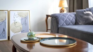 Una mesa ordenada con un hervidor verde, dos platos y arte abstracto enmarcados. Un sofá gris y una lámpara se ven al fondo.